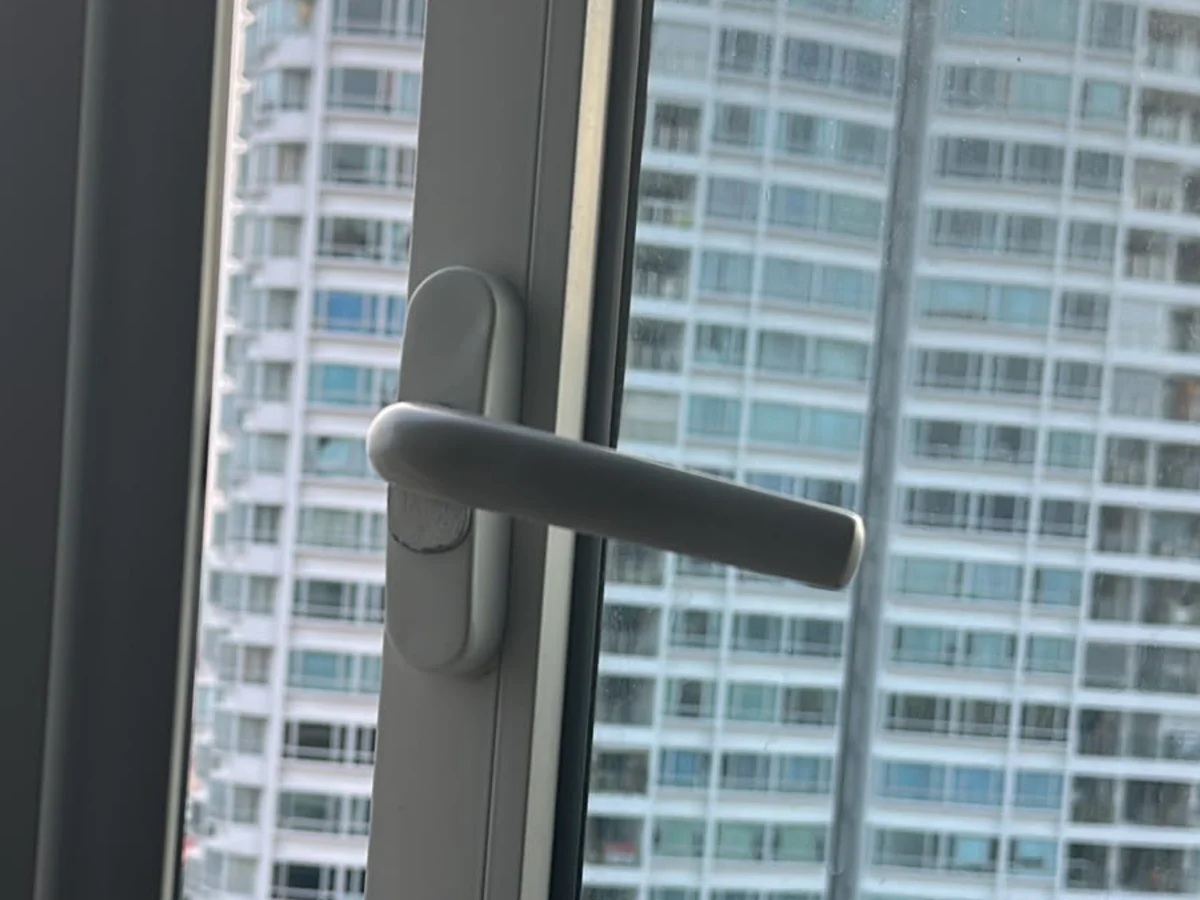White lever handle on an oval backplate, mounted vertically on the edge of an aluminium window sash